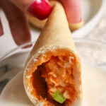 a buffalo chicken empanada being dipped in dressing